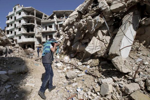 A Syrian covers his face as he walks with a friend between destroyed buildings in the old city of Homs Syria Friday Feb. 26 2016