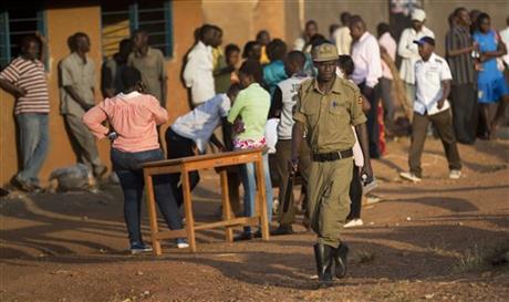 A policeman patrols as voters wait patiently at a polling station where an hour and a half after voting was due to start ballot boxes and papers had not yet arrived in Kampala Uganda Thursday Feb. 18 2016. Ugandans went to the polls Thursday as Presi