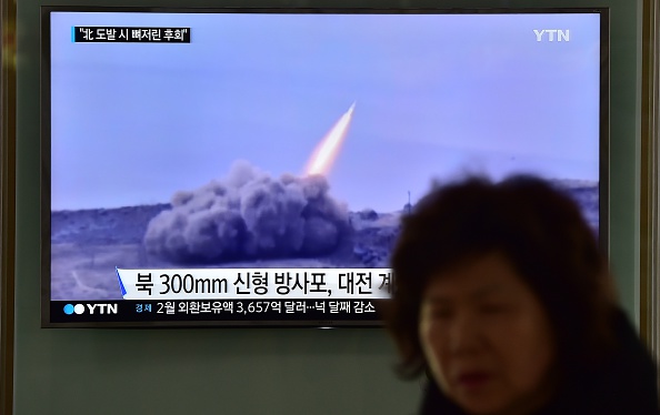 A woman walks past a public television screen showing file footage of a North Korean missile at a railway station in Seoul on March 4