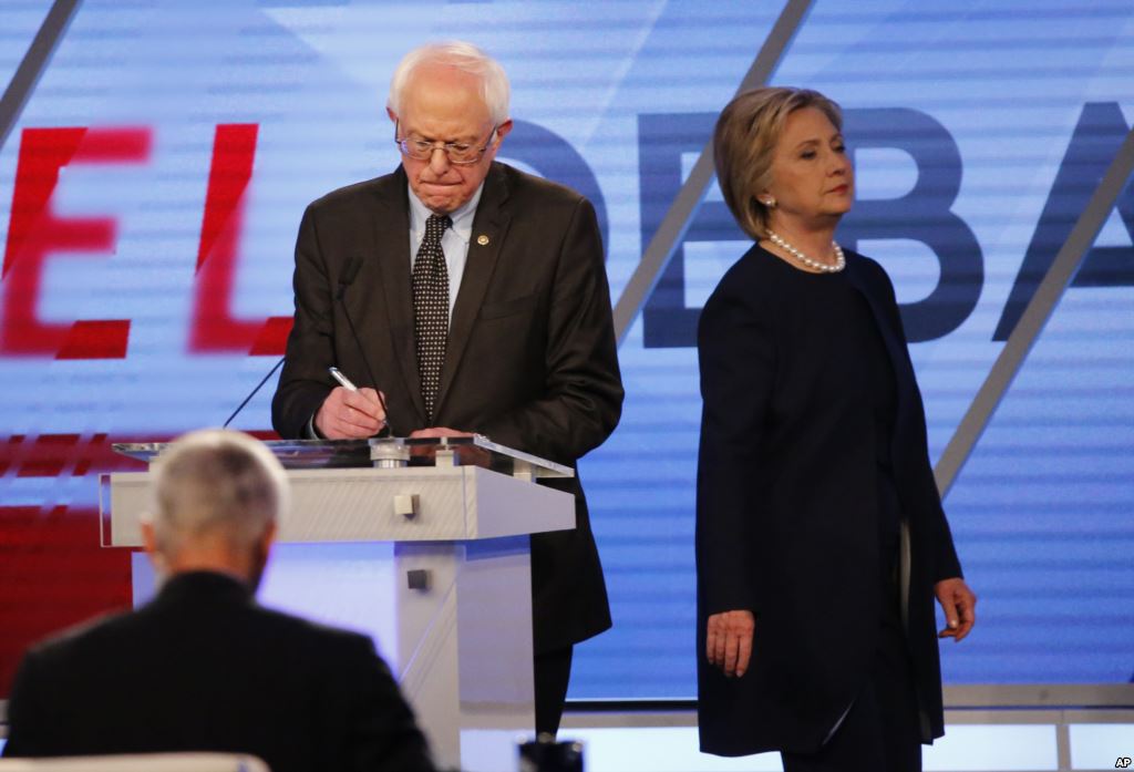 Democratic presidential candidate Hillary Clinton enters the stage after a break as Democratic presidential candidate Sen. Bernie Sanders I-Vt makes notes