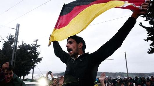 A man holds a German flag as migrants and refugees protest to call for the opening of the borders near the village of Idomeni where thousands of refugees and migrants are stranded on the evening