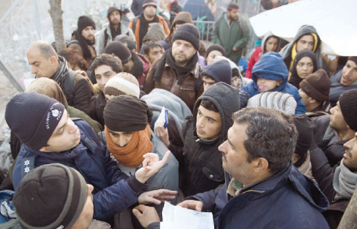 A Greek police officer checks registration papers as refugees crowd to cross the border from the Greek side to Macedonia at the northern Greek border station of Idomeni on Wednesday. — AP