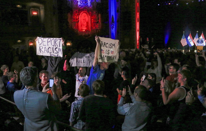 Demonstrators wave signs as they interrupt an election rally of Republican presidential candidate Donald Trump in Kansas City Mo. Saturday