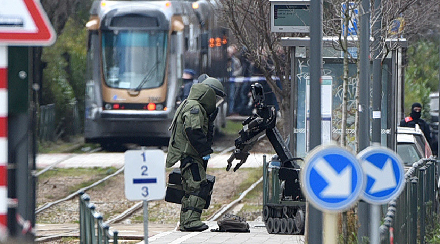 An agent of a bomb squad unit action and a robot stand next to a suspicious object at a tramway station