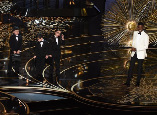 Actor Chris Rock presents children representing accountants from Pricewaterhouse Coopers on stage at the 88th Oscars