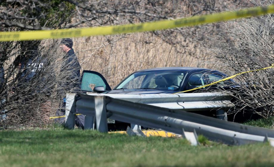 Investigators walk near a car with a shattered window where an off-duty New Jersey police officer was found dead from gunshot wounds in his car in the parking lot of a closed movie theater complex Monday