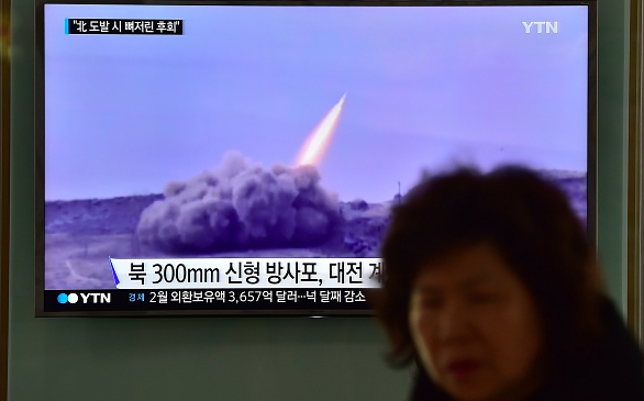 A woman walks past a public television screen showing file footage of a North Korean missile at a railway station in Seoul