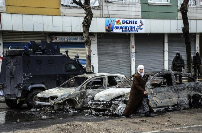 People walk past destroyed vehicles as they leave their houses during clashes in central Diyarbakir