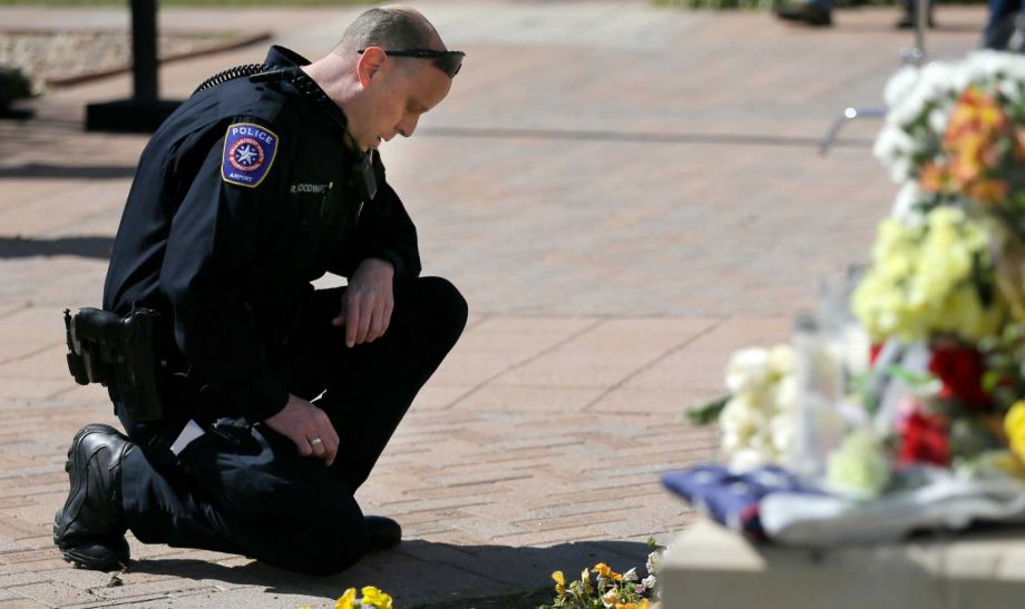 D-FW Airport police Officer Robert Woodward kneels in front of a makeshift memorial for slain Officer David Hofer at the Euless Police Department