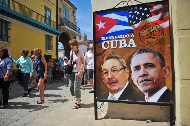 Tourists walk next to a poster of President Castro of Cuba and President Obama in Havana