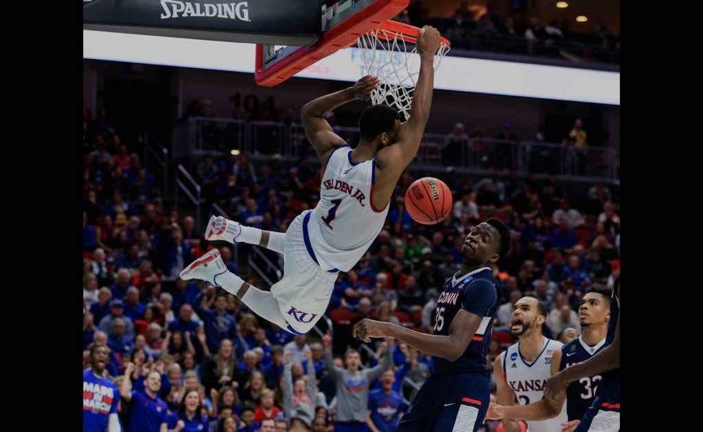 Kansas&#039 Wayne Selden Jr. hangs on to the rim after dunking over Connecticut's Amida Brimah, with Perry Ellis and Shonn Miller watching during a second-round men's college basketball game in the NCAA Tournament in Des Moi