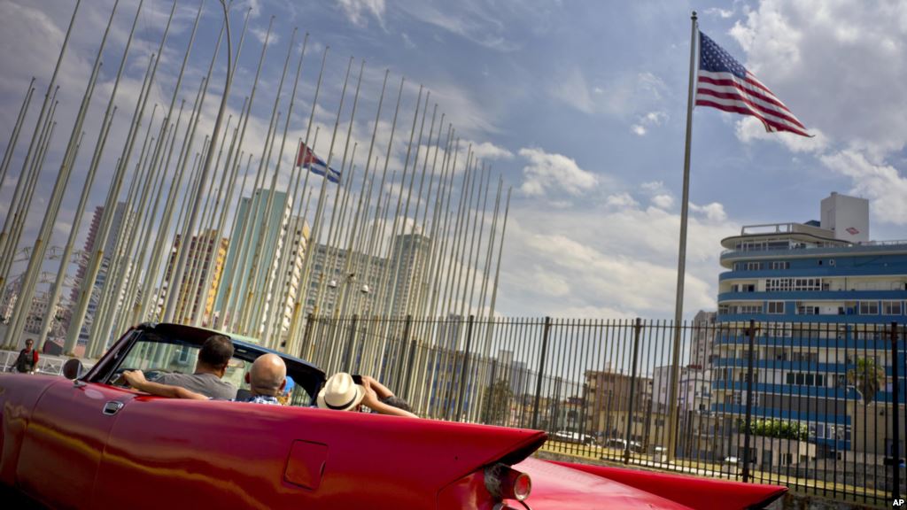 Tourists ride in a vintage American convertible as they pass the U.S. and Cuban flags at the United States embassy in Havana