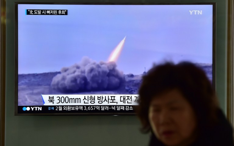 A woman walks past a public television screen showing file footage of a North Korean missile at a railway station in Seoul