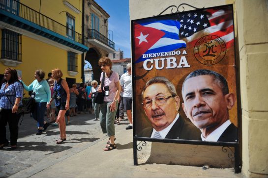 Tourists walk by a poster of Cuban President Raul Castro and U.S. president Barack Obama in Havana Friday. While the visit is unlikely to yield any big announcements it allows both leaders to set in place the next steps for Cuba and the U.S. to deal with