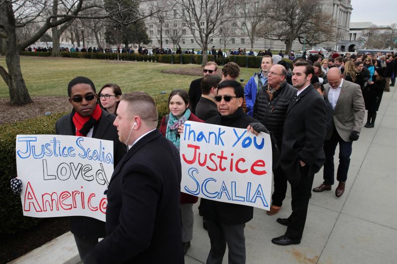 People hold signs of thanks and support while waiting in line to pay their respects