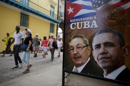 Tourists pass by images of U.S. President Barack Obama and Cuban President Raul Castro in a banner that reads