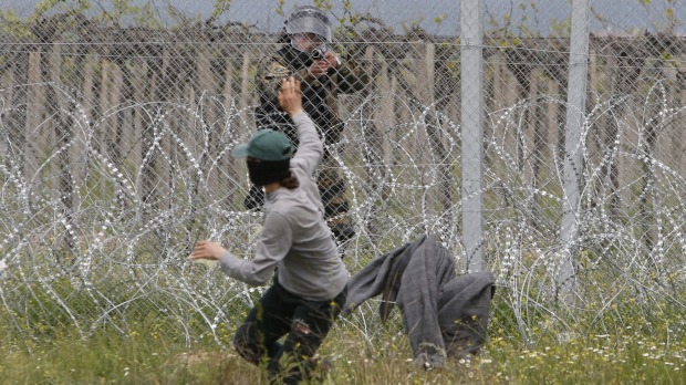 A Macedonian police officer takes aim at a migrant who had been trying to remove barbed wire along the border with Greece