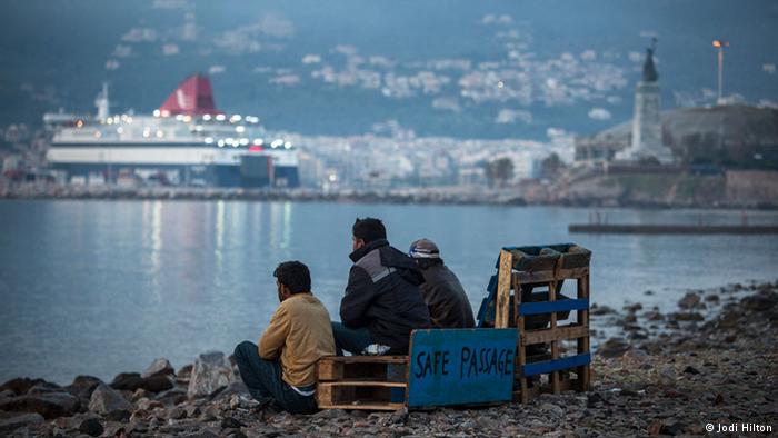 Pakistani migrants sit on a Lesbos beach next to a sign reading Safe passage and looking out at the water