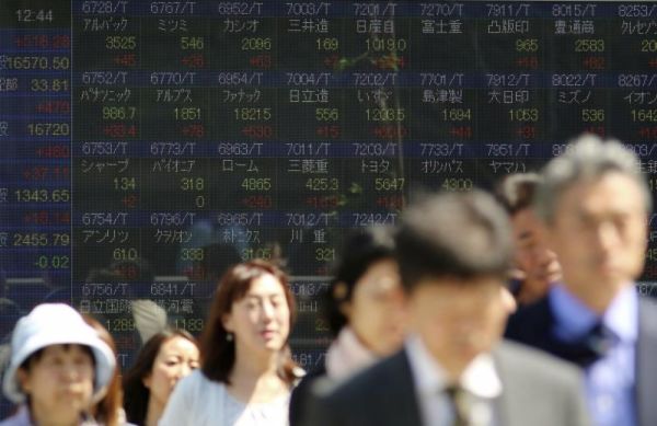 People walk past an electronic stock board showing