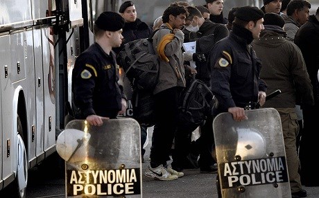 Greek police stand guard as deported migrants board a boat. AFP