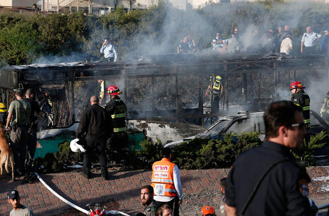 Israeli security forces and emergency services gather around a burnt-out bus following an explosion by IED