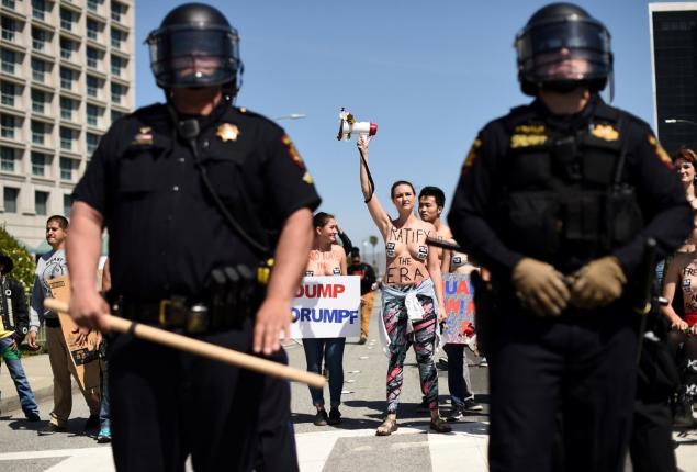 NOAH BERGER  REUTERS  Topless demonstrator Rebecca Marston holds up a bullhorn behind police in riot gear