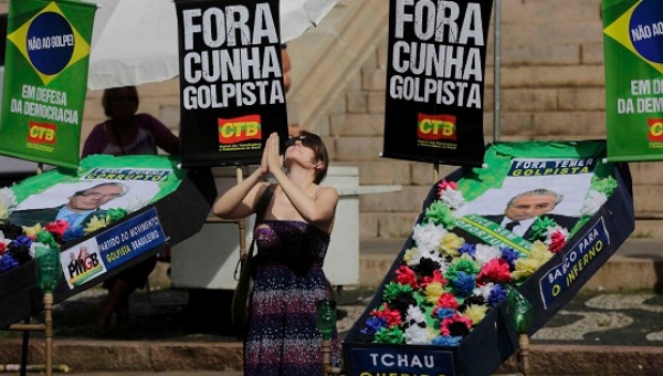 A protester kneels with mock coffins of house speaker Eduardo Cunha and Vice President Michel Temer with'Out coup-plotter signs in Porto Alegre