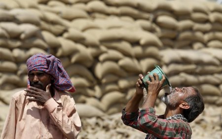 A labourer drinks water as another looks on on a hot summer day at a grain market in Chandigarh India