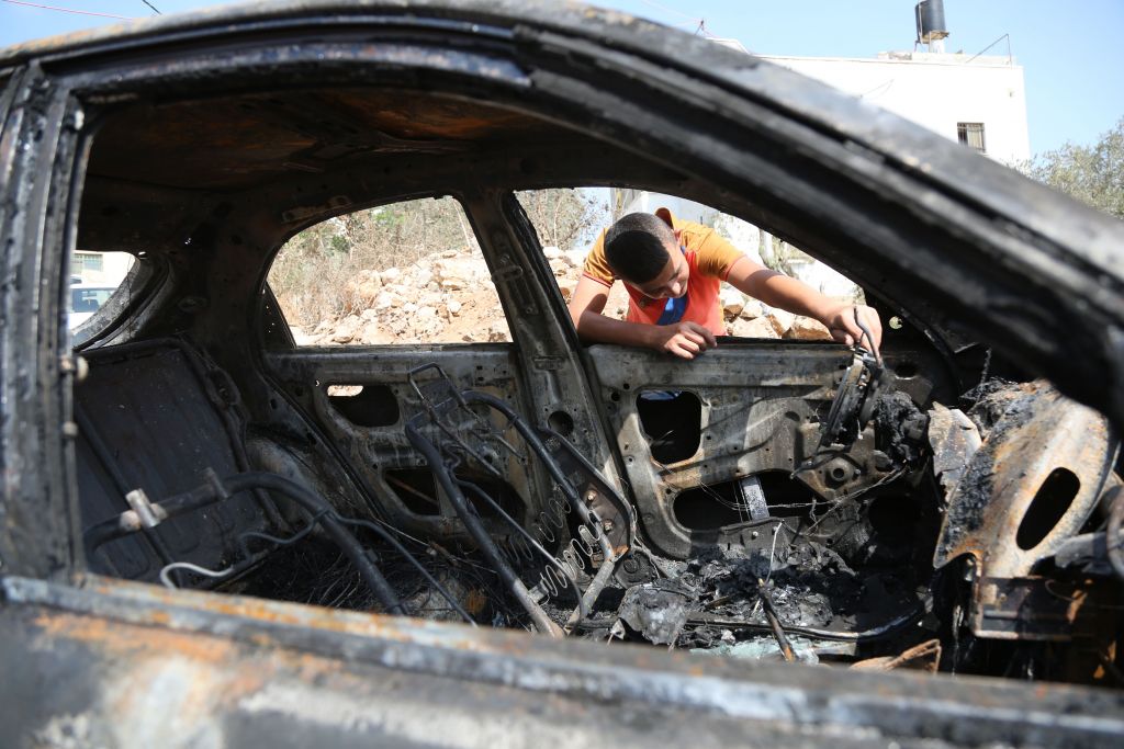 Illustrative A Palestinian boy looks at a car belonging to Palestinians which residents said was burnt by Jewish settlers in a village near the West Bank city of Ramallah