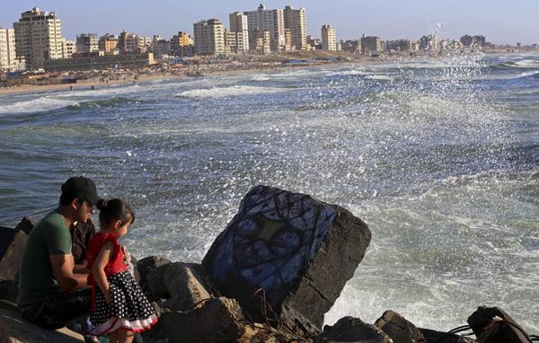 A Palestinian man sits with his children on the shore of the Mediterranean Sea in Gaza City on Thursday