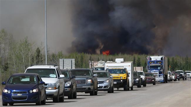 A convoy of evacuees drives south as flames and smoke rises along the highway near Fort McMurray Alberta Canada