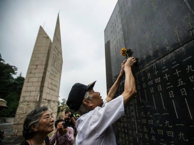 A man places a flower on a monument in Nanjing showing the names of people who died in battles against Japan during World War II