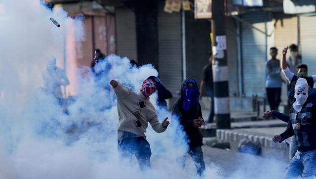 A masked protester throws back an exploded tear gas shell at Indian policemen during a protest in Srinagar on April 12