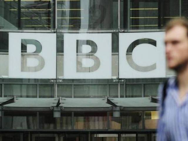 A pedestrian walks past a BBC logo at Broadcasting House in central Lond