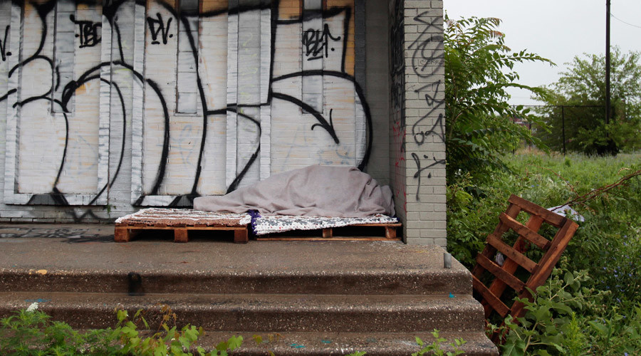 A homeless person sleeps under a blanket on the porch of a shuttered public school covered with graffiti in a once vibrant southwest neighborhood in Detroit