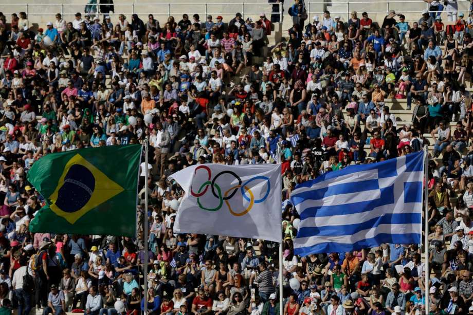 The flags of Greece right Brazil left and Olympics wave as spectators wait for the handover ceremony at Panathinean stadium in Athens Wednesday