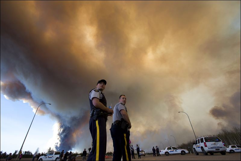 Police officers direct traffic under a cloud of smoke from a wildfire in Fort McMurray Alberta Friday. Officials said shifting winds were giving the embattled northern Alberta city a break but they added the fire that forced 80,000 people from their hom