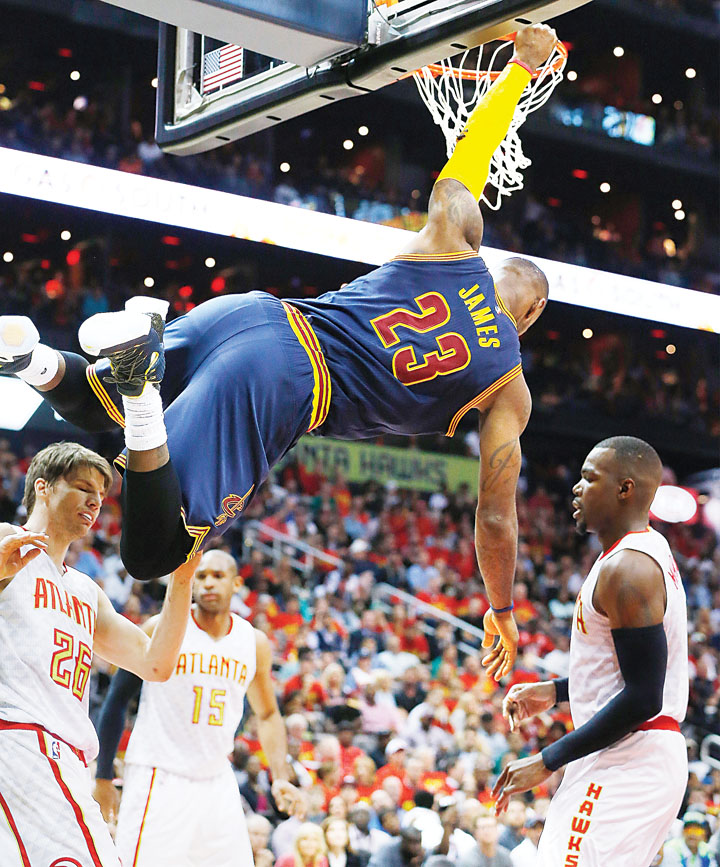 LeBron James of the Cleveland Cavaliers hangs on the rim after scoring a dunk while Paul Millsap and Kyle Korver of the Atlanta Hawks look on during the Cavaliers’ 100-99 victory that earned them a slot in the NBA Eastern Conference Finals