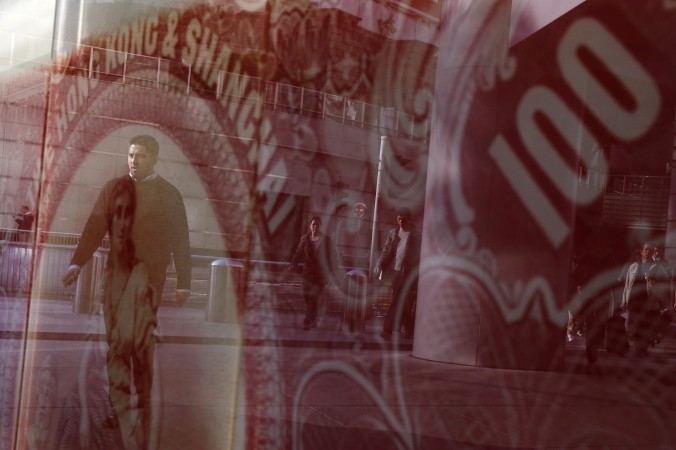 People are reflected on a glass case displaying a poster featuring a 100 dollar Hong Kong colonial bank note in Hong Kong