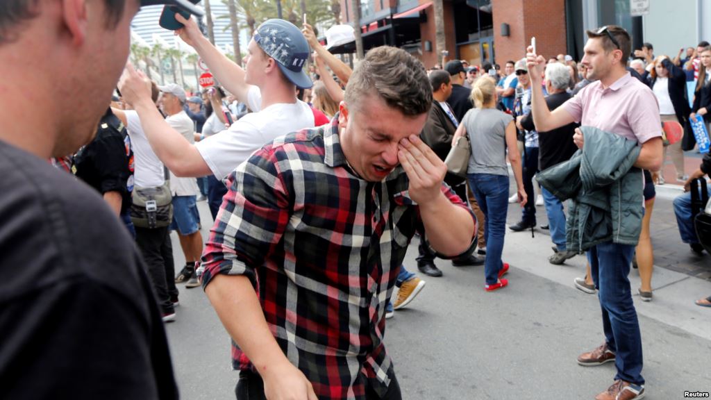 A man holds his face after being hit with pepper spray during a demonstration outside a campaign event for Republican presidential candidate Donald Trump in San Diego Calif