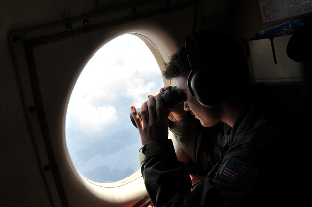 U.S. Navy LT. JG Dylon Porlas uses binoculars to look through the window of a U.S. Navy Lockheed P-3C Orion patrol aircraft from Sigonella Sicily Sunday M