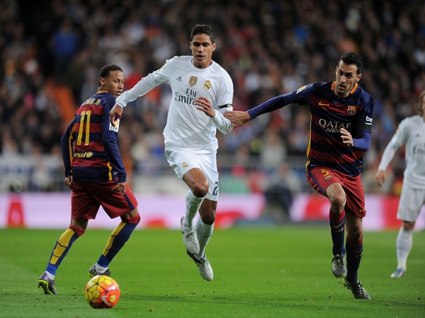 Real Madrid center back Raphael Varane competes for the ball against Barcelona's Sergio Busquets and Neymar