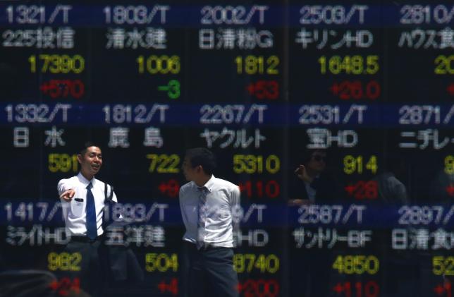 Men are refelcted in a screen displaying market indices outside a brokerage in Tokyo Japan