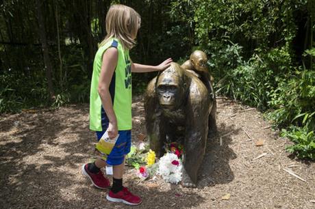 A child touches the head of a gorilla statue where flowers have been placed outside the Gorilla World exhibit at the Cincinnati Zoo & Botanical Garden Sunday