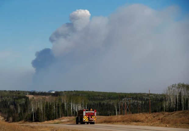 A fire truck drives down a highway in front of the Fort Mc Murray wildfires in Kinosis