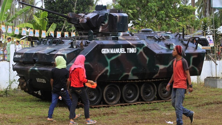 Residents walk past a military tank outside a polling station in the town of Pantar Lanao del Norte province on the southern Philippine island of Mindanao