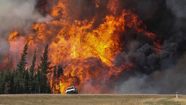 Smoke and flames from the wildfires erupt behind a car on the highway near Fort McMurray Alberta Canada