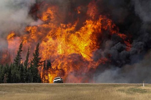 Smoke and flames from the wildfires erupt behind a car on the highway near Fort McMurray Alberta Canada