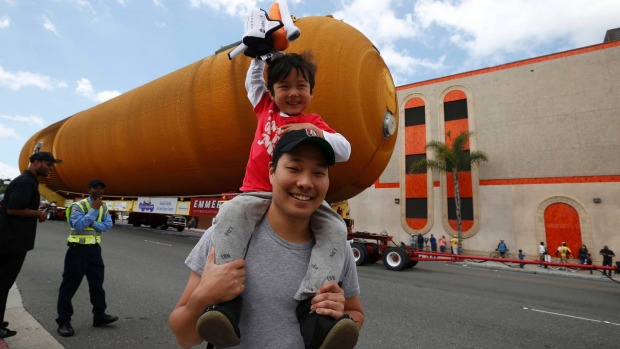 Four-year-old Hudson Lee waves a toy space shuttle while sitting on his father Eddie Lee's shoulders as the space