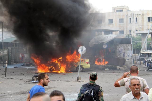 A Syrian army soldier and civilians inspect the damage after explosions hit the Syrian city of Tartous in this handout